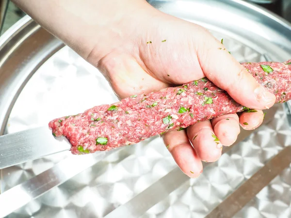 A chef making shish kebab of red meat with parsley over metal pl