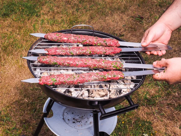 A chef putting red meat shish kebab onto a charcoal barbecue