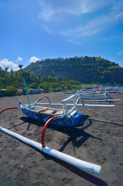 Local  boats on the beach of black sand on the island of Bali in