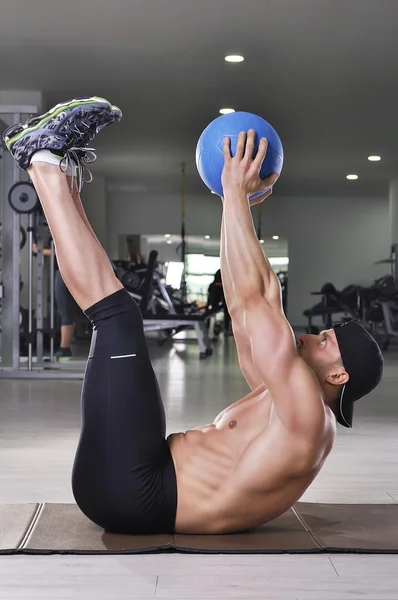 Handsome powerful athletic man performing crunches with medicine ball. Strong bodybuilder with perfect abs, arms and back.