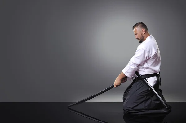 Handsome young black belt male karate posing with sword on the gray background