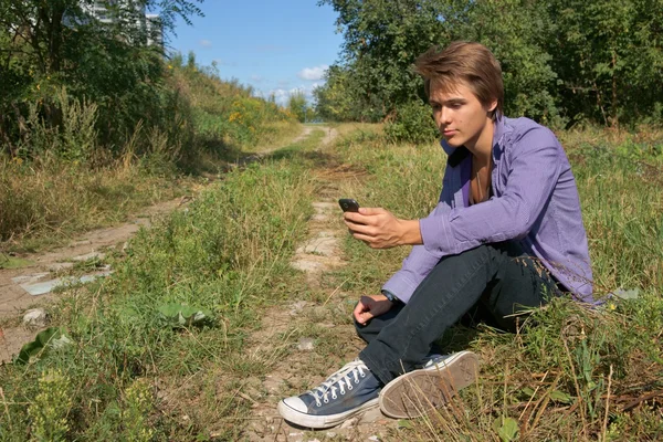 Teenage boy sitting on the grass and using mobile phone