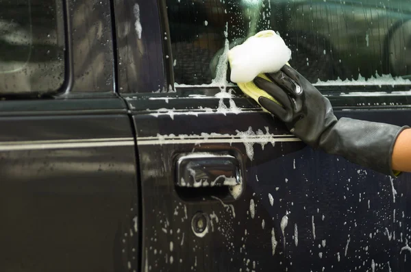 Closeup black rubber gloves working on washing car door window with soapy water