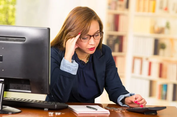 Business woman wearing glasses sitting by desk with computer expressing mild frustration