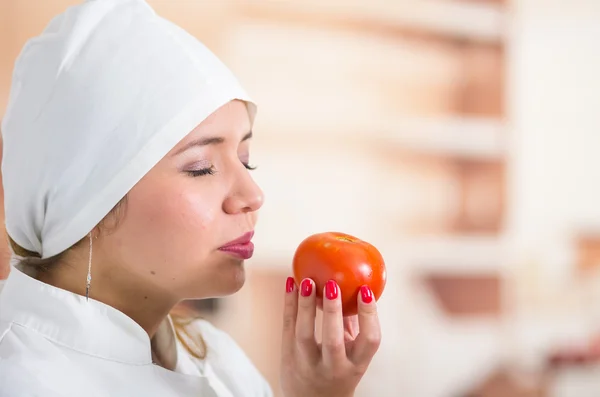Closeup headshot of woman chef holding up a tomato and smelling it with her eyes closed