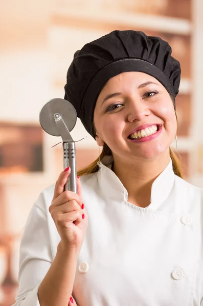 Woman chef wearing cooking outfit posing happily holding metal pizza cutter