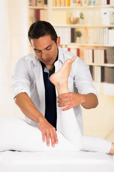 Male physio therapist hands working on female patients legs, holding and bending, blurry clinic background