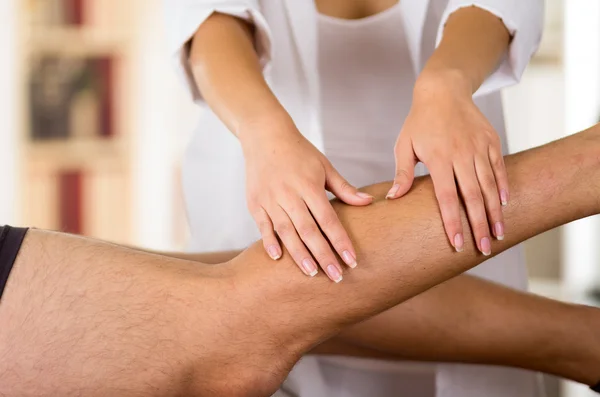 Closeup female physio therapist hands working on male patients legs, blurry clinic background