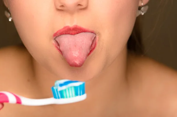 Closeup young womans open mouth with tongue sticking out and toothbrush in front