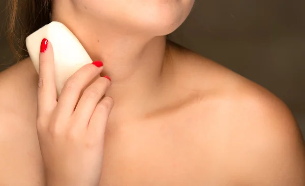 Closeup young womans bare skin shoulders and upper chest, rubbing bar of soap on body