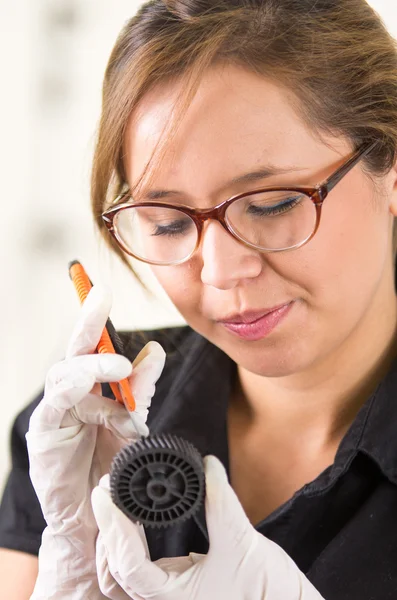 Young woman wearing black shirt holding up toner parts and looking closely into it while performing maintenance, concentrated facial expressions