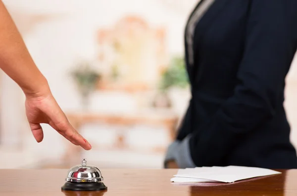 Closeup customer guest hand reaching for traditional reception bell with uniformed employee in background