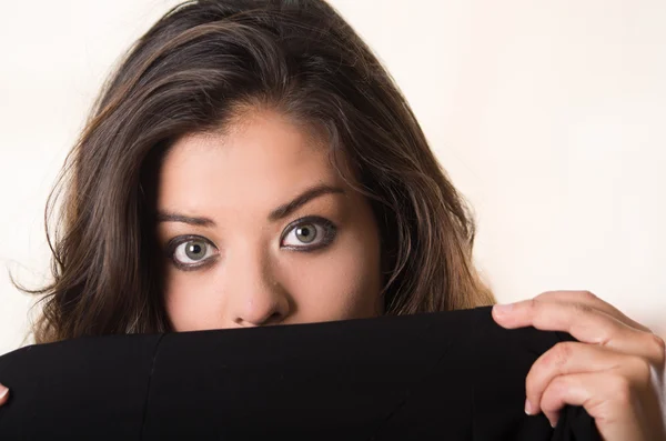 Headshot attractive brunette facing camera covering half her face with black clothing, white studio background