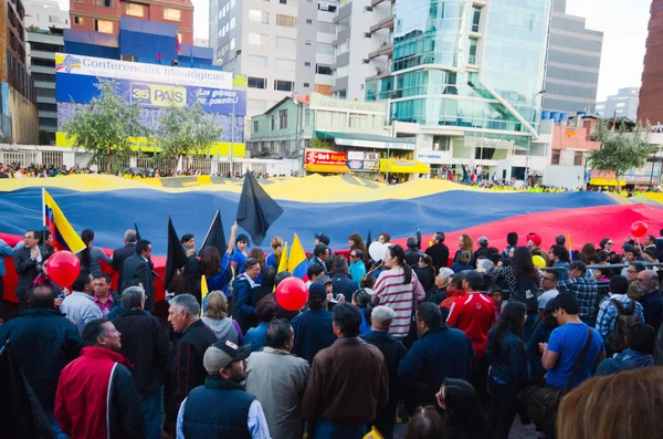 Quito, Ecuador - April 7, 2016: Group of people displaying a very big Ecuadorian Flag, protest signs, and journalists during anti government protests in Shyris Avenue.