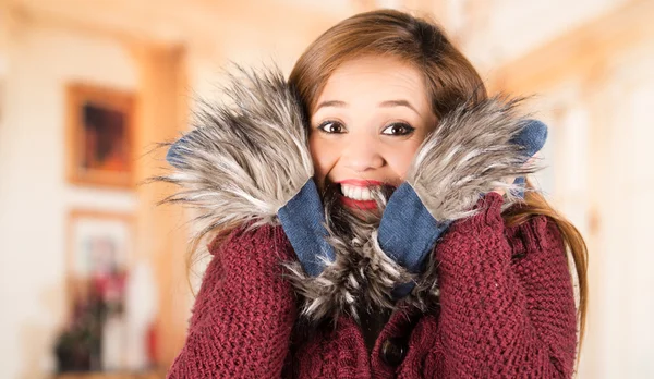Pretty young brunette woman squeezing her head between large blue scarf and smiling, freezing cold concept