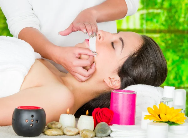 Woman headshot profile, lying with eyes closed and hand applying wax paper to upper lip of client