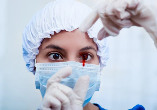 Closeup headshot nurse wearing bouffant cap and facial mask holding up blood sample on slide glass for camera