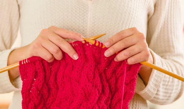 Closeup womans hands holding wooden knitting needles working on red scarf