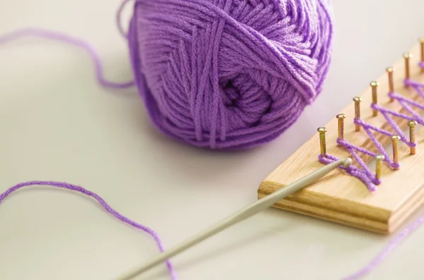 Purple yarn ball  on white surface, loose end tied up to wooden board with nails, handcraft textile concept