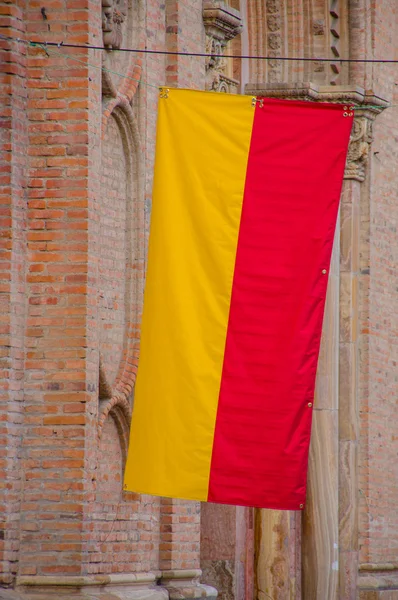 Cuenca, Ecuador - April 22, 2015: Closeup yellow and red Cuenca flag hanging down from pole attached to brick building