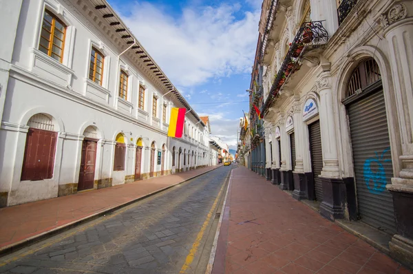 Cuenca, Ecuador - April 22, 2015: Charming city streets with typical red sidewalks and narrow car road, white spanish colonial architecture buildings on both sides, Cuenca flag hanging from wall