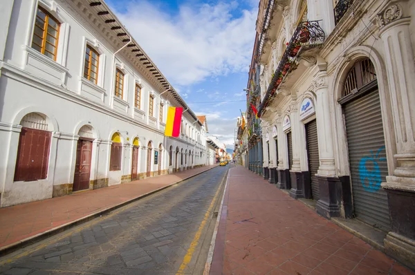 Cuenca, Ecuador - April 22, 2015: Charming city streets with typical red sidewalks and narrow car road, white spanish colonial architecture buildings on both sides, Cuenca flag hanging from wall