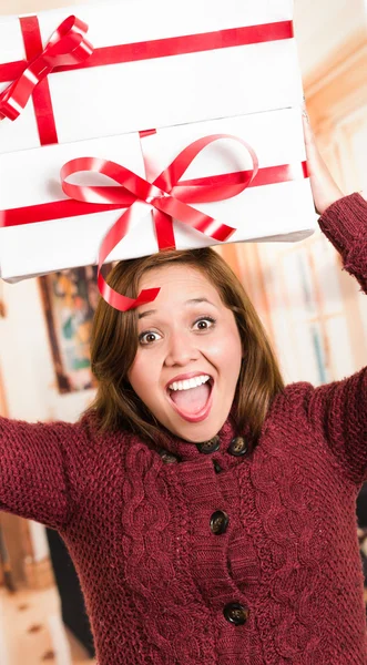 Brunette with beautiful smile holding up presents above head happily posing for camera, white wrapping and red ribbon, household background