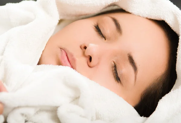 Closeup headshot young woman lying down comfortably, eyes closed with head covered in white towels