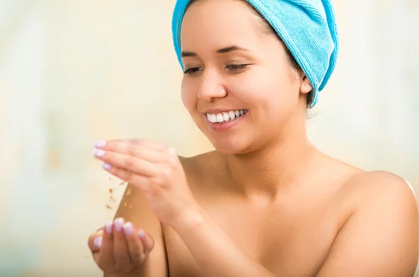 Pretty young healthy hispanic woman headshot with naked shoulders, blue towel wrapped around head, posing happily, creamy hands