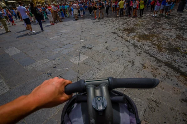 FLORENCE, ITALY - JUNE 12, 2015: Bycicle handlebars with one hand ridding close up, stone wet street with a lots of people in front