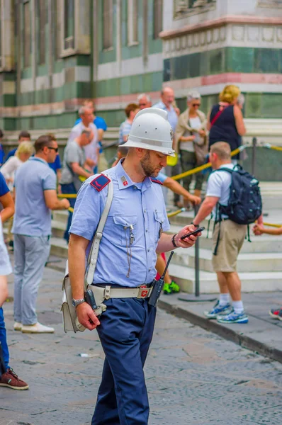 FLORENCE, ITALY - JUNE 12, 2015: Handsome italian police crossing the street looking at his mobile phone