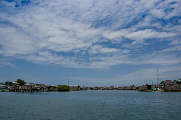 Muisne, Ecuador - March 16, 2016: Muisne town as seen from water, modest wooden houses sitting on poles waterfront pacific ocean, city buildings background and beautiful blue sky