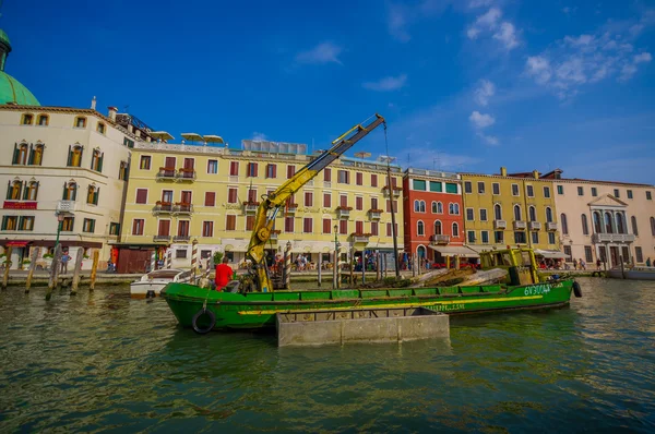 VENICE, ITALY - JUNE 18, 2015: Green boat with a crane parking in Venice canals, equipment to help