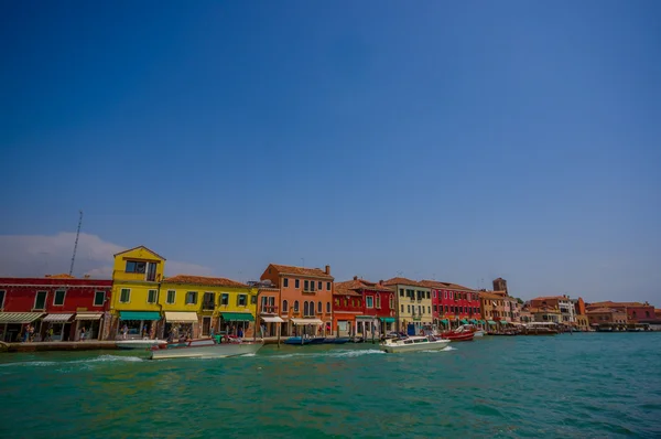 MURANO, ITALY - JUNE 16, 2015: Panoramic view of little colored houses at Murano on the river border, boat passing on the water