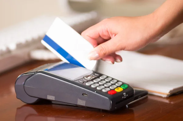 Credit card machine close up, white card with blue band swiping in the machine, woman hand