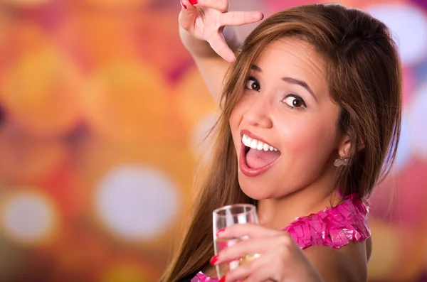 Happy woman making peace and love expression hand and holding champagne cup with other hand, colored background