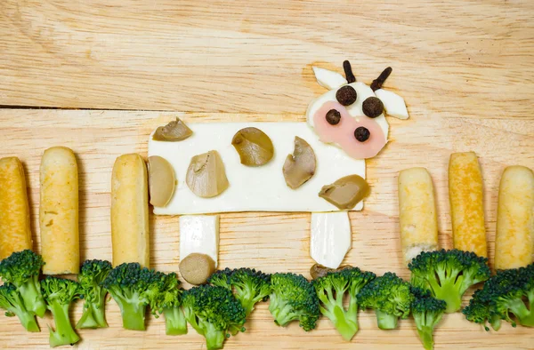 Cow with landscape made from cheese, white carrots, broccoli, mushroom and ham, artistic food concept