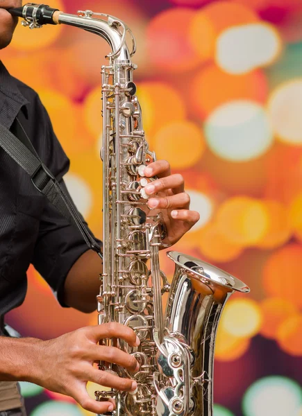 Man wearing dark shirt playing saxophone, blurry lights background and seen from profile angle