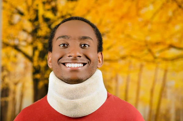 Injured young positive black hispanic male wearing neck brace and smiling to camera, yellow abstract background