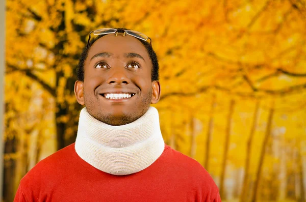 Injured young positive black hispanic male wearing neck brace and smiling to camera, yellow abstract background