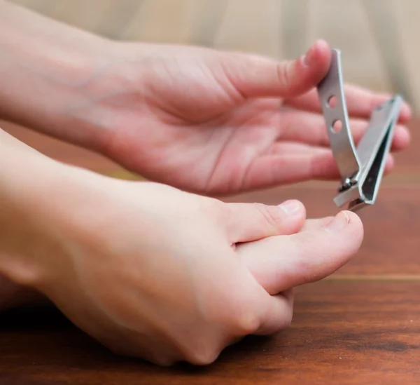 Metal clipper cutting feet nails, hands helping in a wooden background