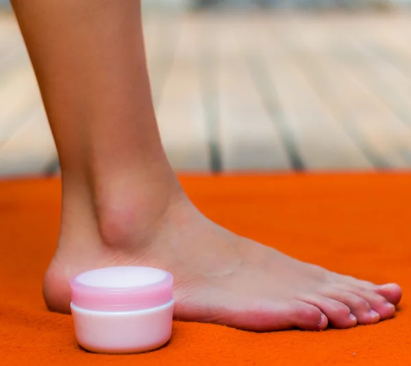 Clean and nice feet on an orange background, a pot of pink cream on the side
