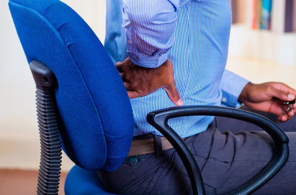 Man apparently working, sitting in a chair and holding his back, pain signal