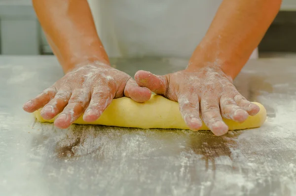 Hands of baker working, kneading and rolling bread dough, shaping into loaf before cooking