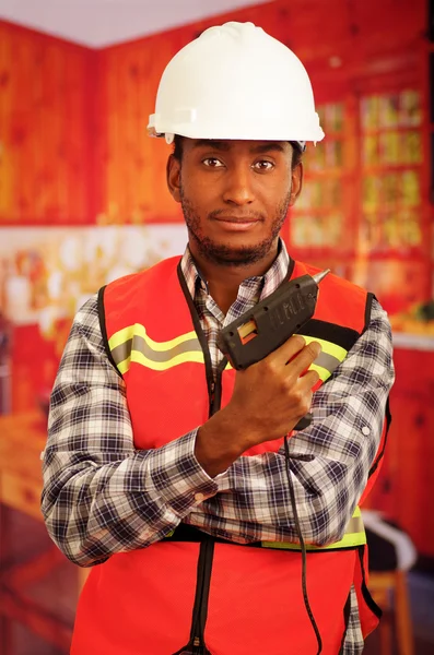 Young engineer carpenter wearing square pattern flanel shirt with red safety vest, holding glue gun smiling to camera