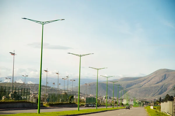 Great landscape from highway point of view showing mountains in distance, green lamp posts and blue skies