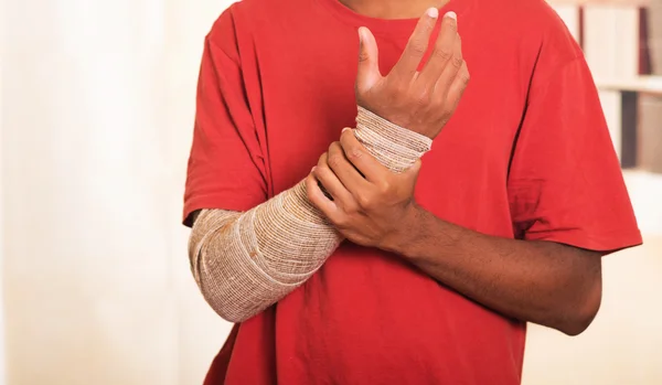 Closeup man in red shirt wearing large grey bandage over lower right arm, supporting with other hand
