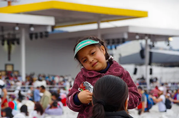 QUITO, ECUADOR - JULY 7, 2015: Confused face of a girl with a little hat waitting in the mass of pope Francisco event, chips in her hands