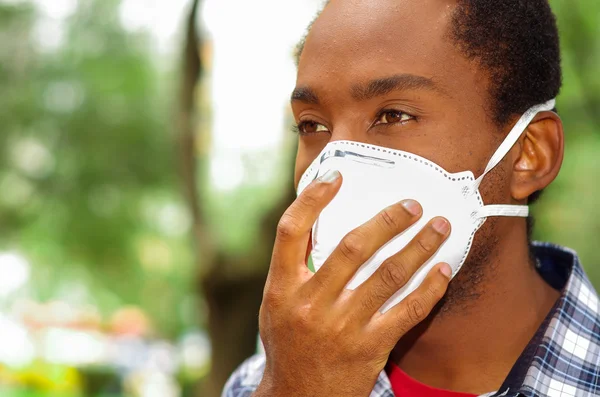 Closeup man headshot covering nose and mouth with protection filter mask walking outside, blurry trees background