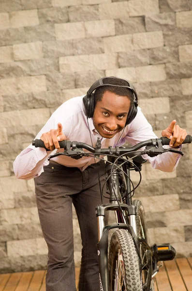 Man wearing grey office pants, white red business shirt standing by bicycle in racing position smiling, brick wall background